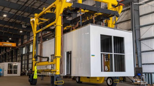 A power generation enclosure being transported through ASC's manufacturing warehouse using a straddle carrier.